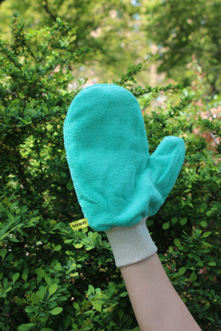Green TiCK MiTT glove held in front of a green bush